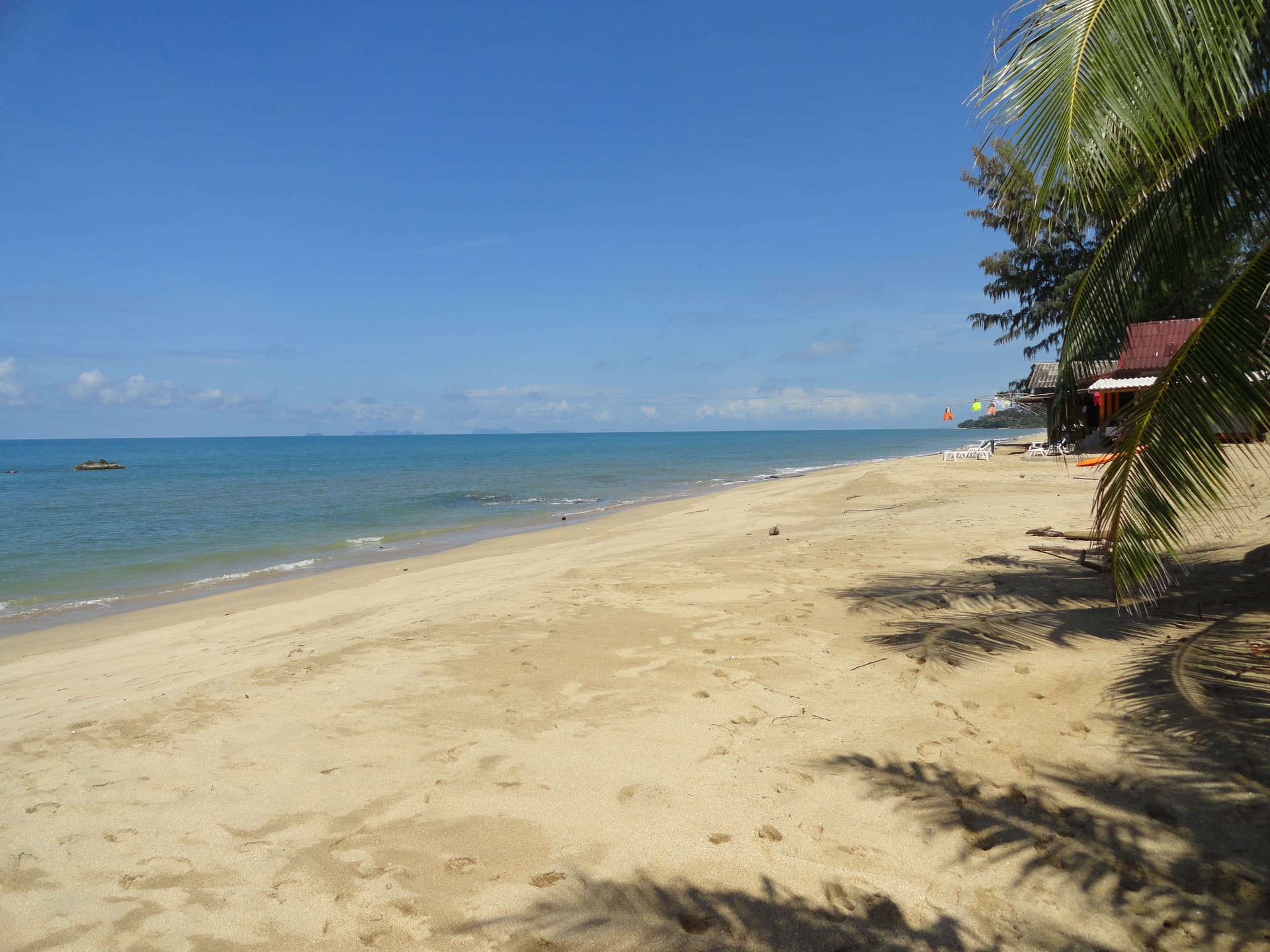 A quiet west-coast beach on Koh Lanta with longtail boats and palm trees